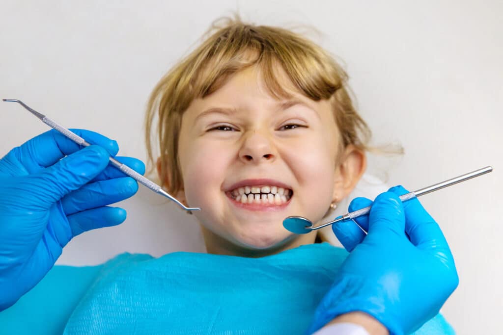 Young child smiling during dental examination with dentist holding tools in Puyallup.