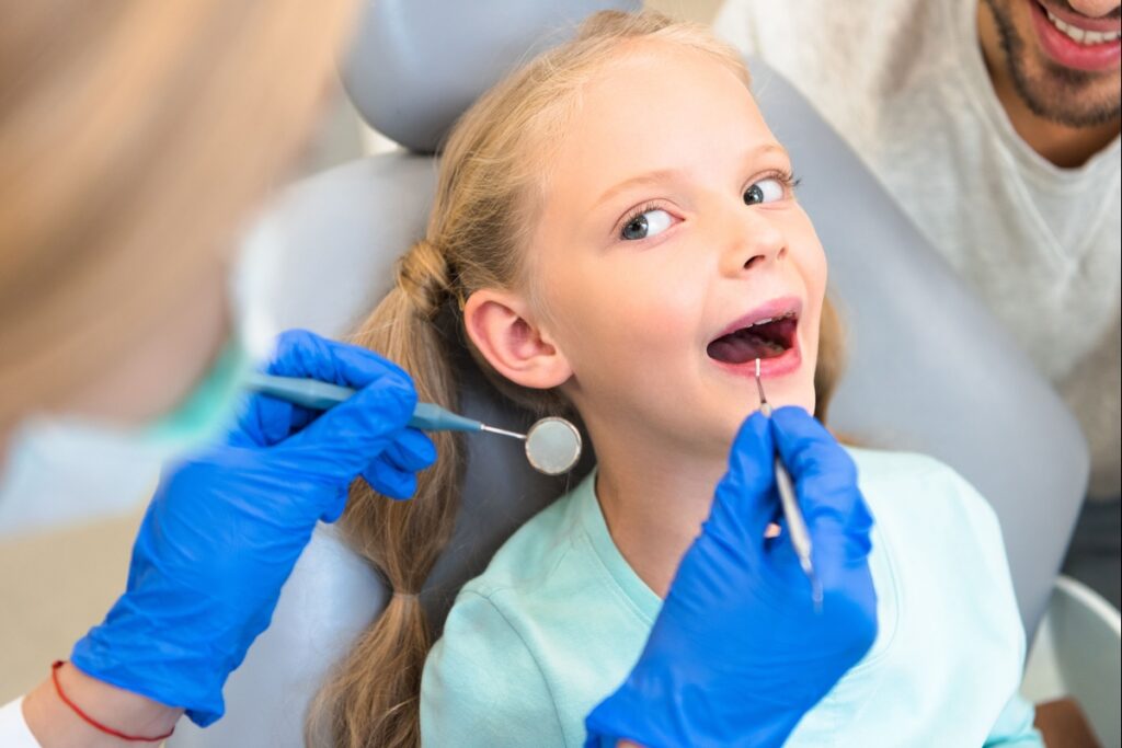 Young girl receiving dental examination with dentist using mirror and explorer in operatory.