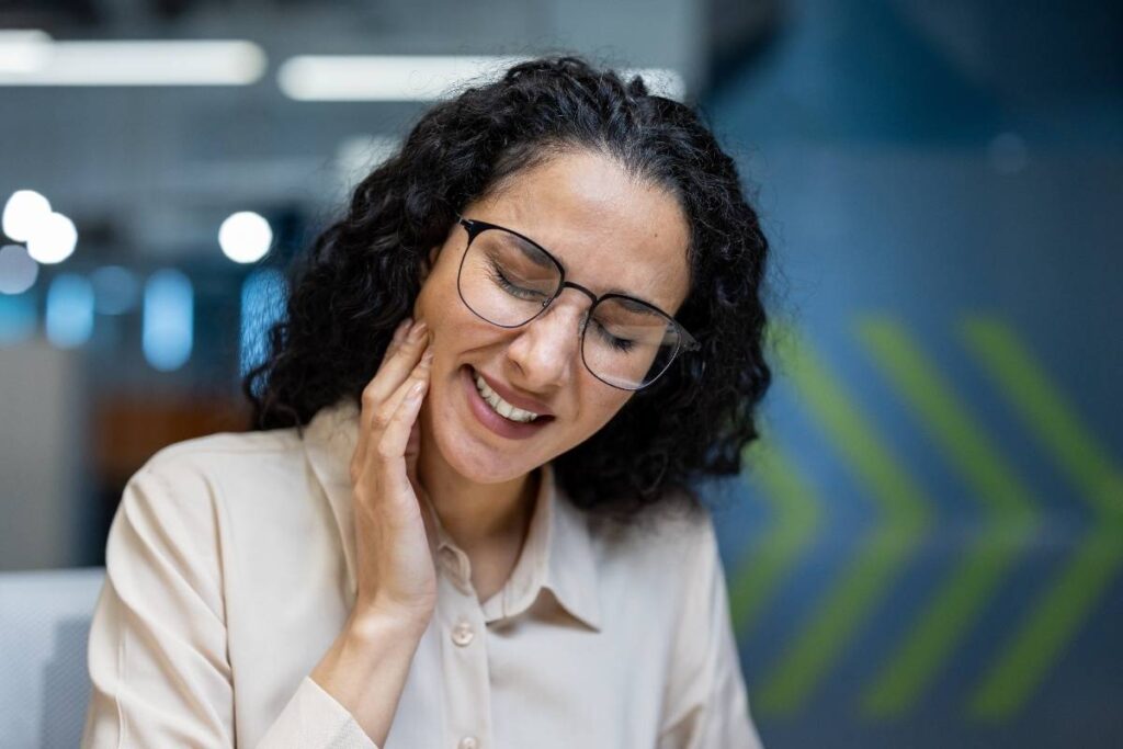 Woman with curly dark hair and glasses smiling at a dental office.