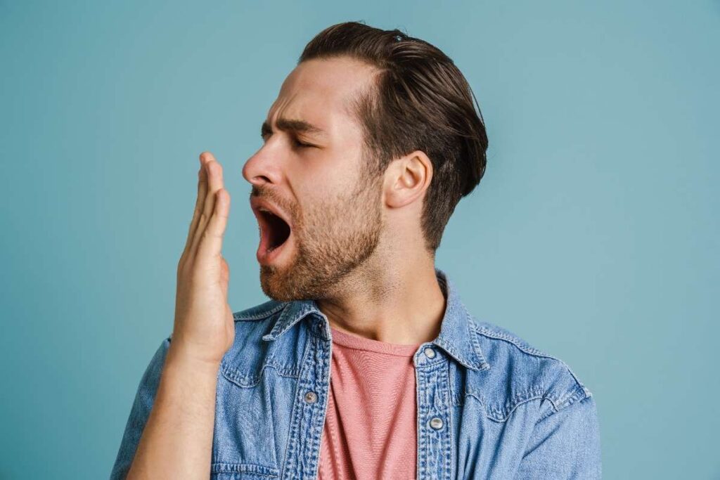 Man checking breath with hand near mouth against blue background.