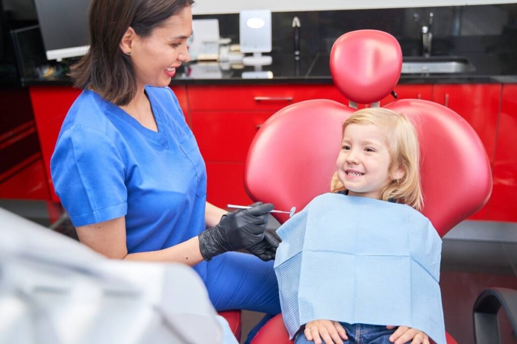 Pediatric dentist in blue scrubs consulting with smiling young patient in Puyallup dental office.