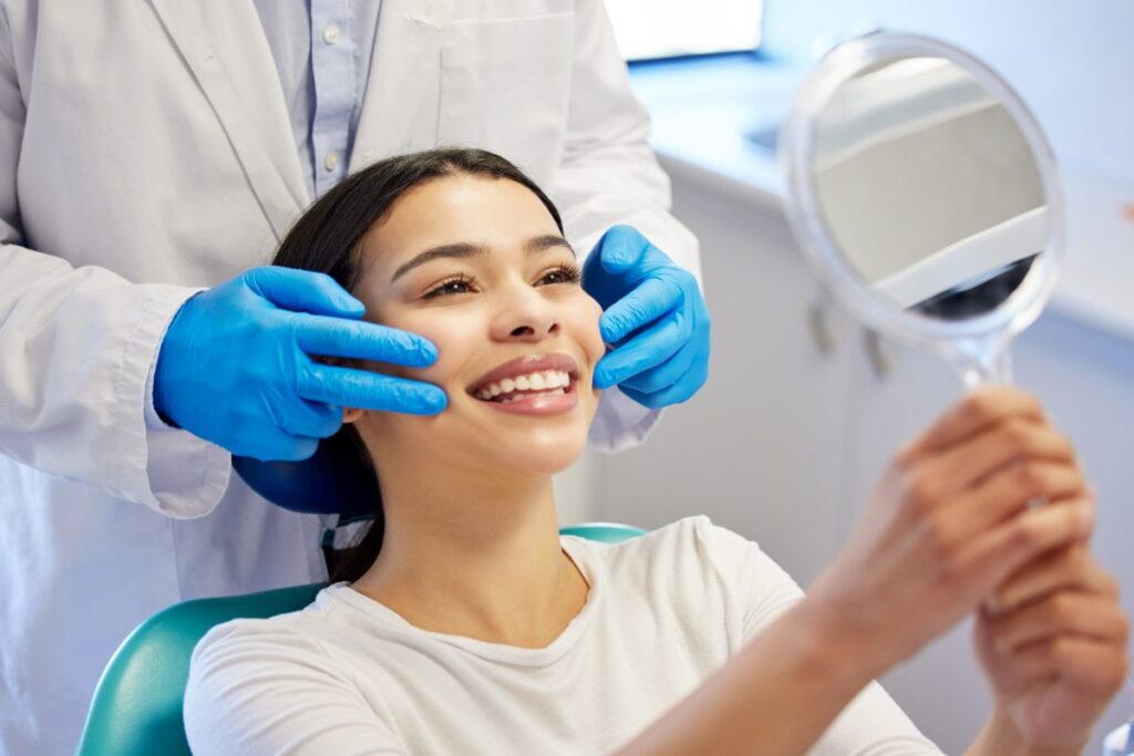 Young woman smiling at dental mirror while dentist examines her teeth in Puyallup office.