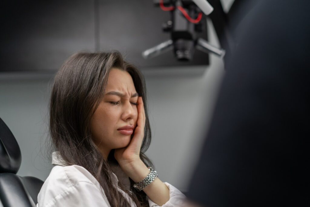 Woman in dental office experiencing tooth pain, holding her cheek during emergency dental consultation.